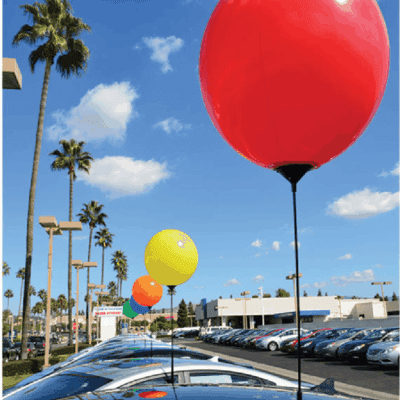 Colorful balloons on poles above parked cars in a dealership setting, enhancing visibility and attracting attention to automotive supplies.