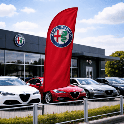 Alfa Romeo red flag displayed outside a dealership, featuring the Alfa Romeo logo, with several Alfa Romeo cars parked in front of the modern dealership building.
