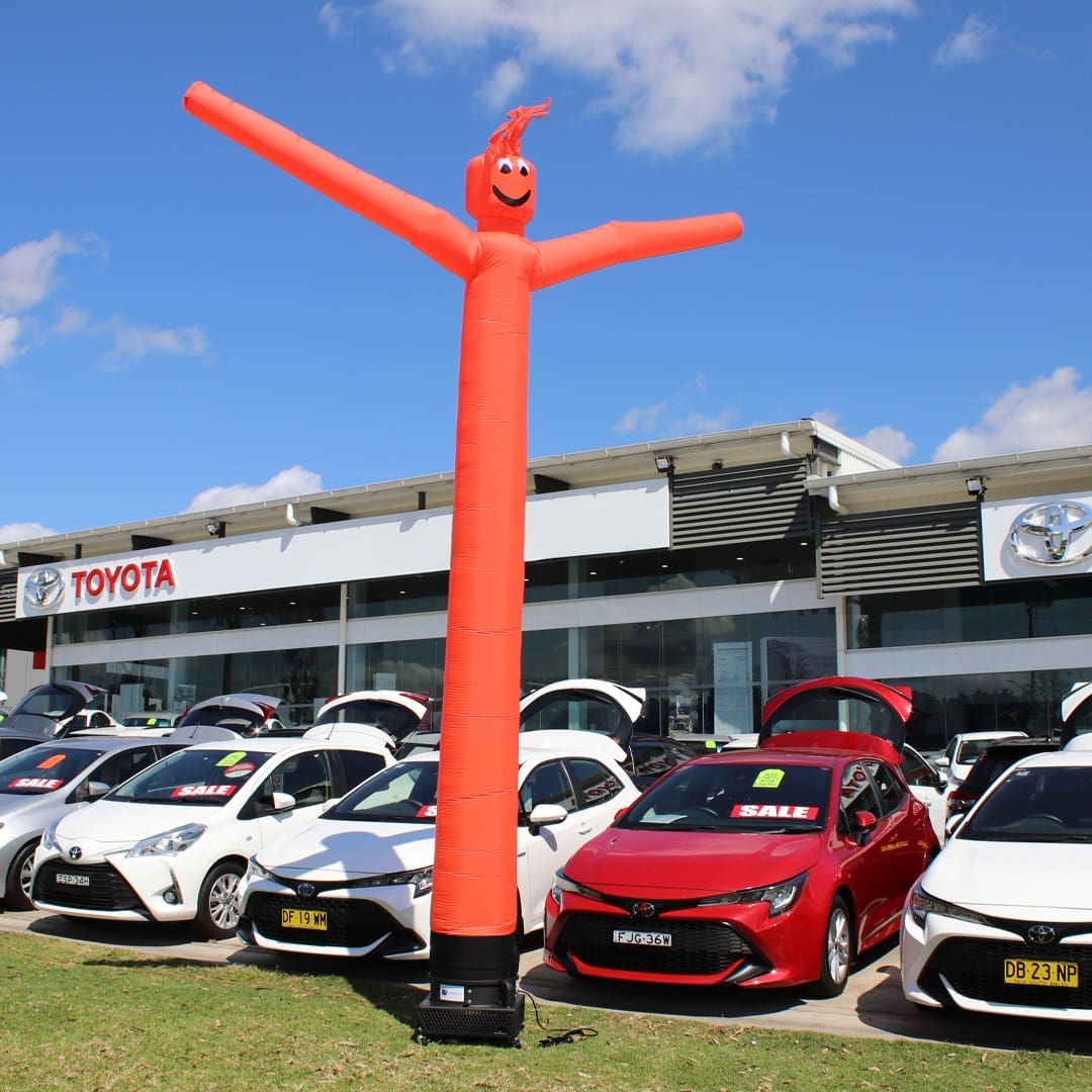 Red inflatable advertising man waving in front of Toyota car dealership.