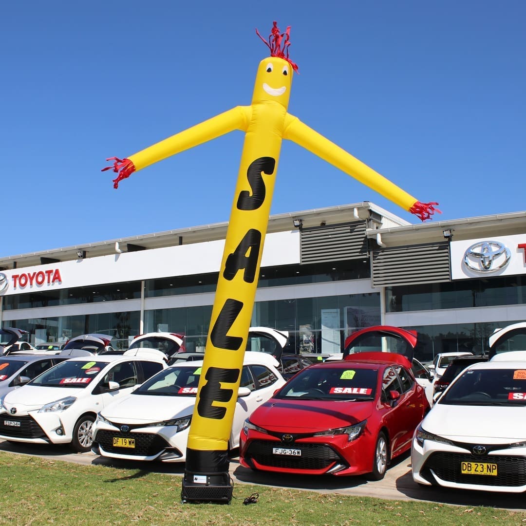 112SAYB1 Yellow inflatable advertising man waving in front of Toyota car dealership and vehicles