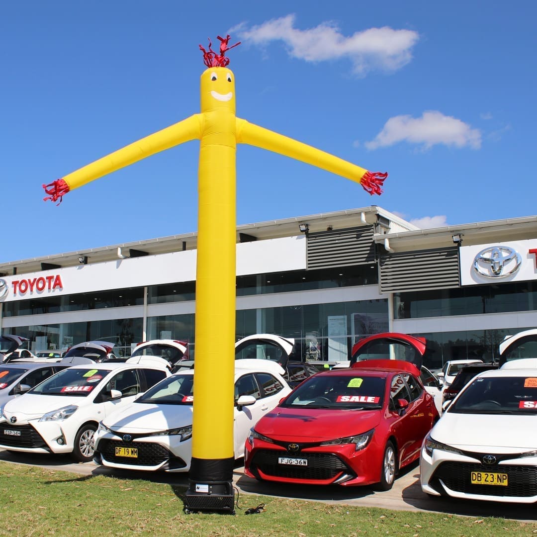 112Y1 Yellow inflatable advertising man waving in front of Toyota car dealership.