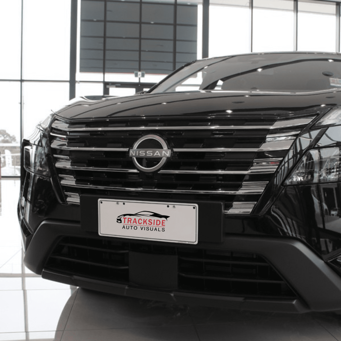 Nissan vehicle front view showcasing Trackside Auto Visuals license plate in a dealership setting.