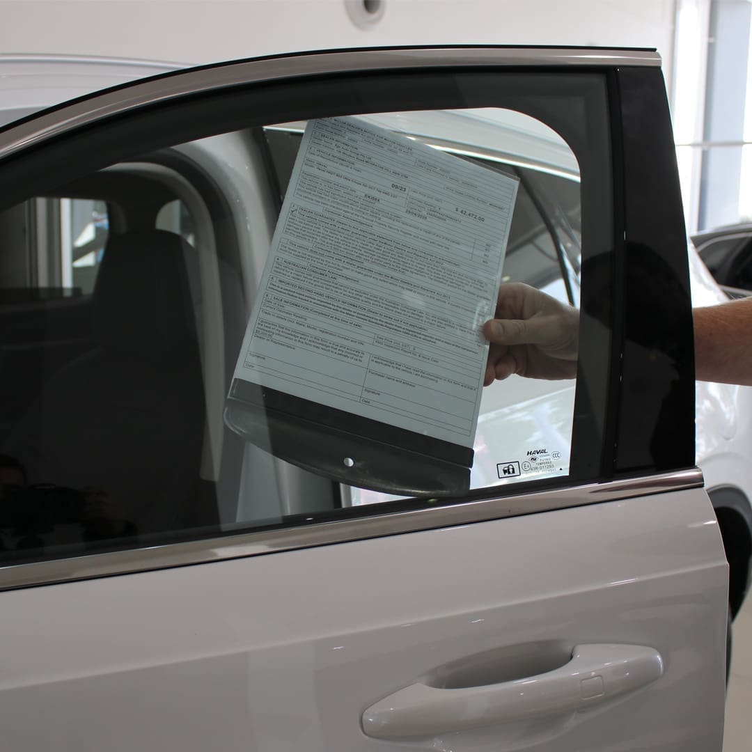 Hand placing a slide-in form holder with informational document inside a car window at a dealership, showcasing car dealership supplies.